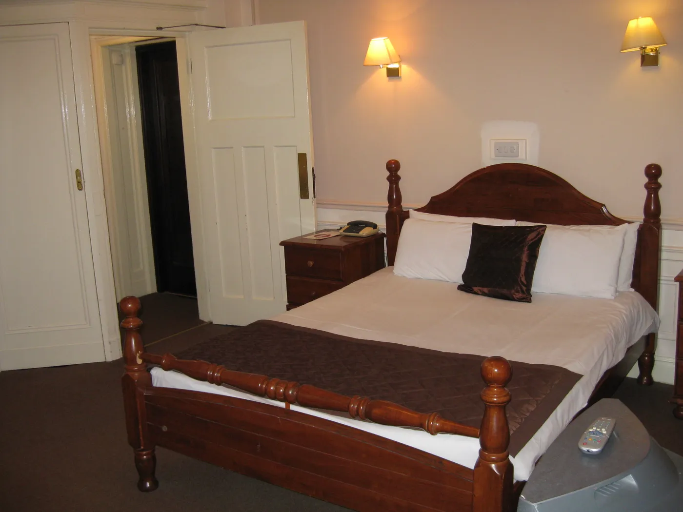 A double bed with a dark wooden headboard and bedside table in a bedroom at the Adelphi Hotel