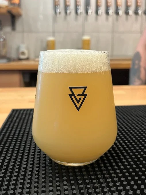 Freshly poured glass of hazy pale ale with Azvex triangle logo on the bar drip mat