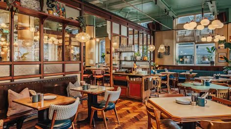 Dishoom Permit Room dining room with warm lighting, wooden floors and tables set for a meal.