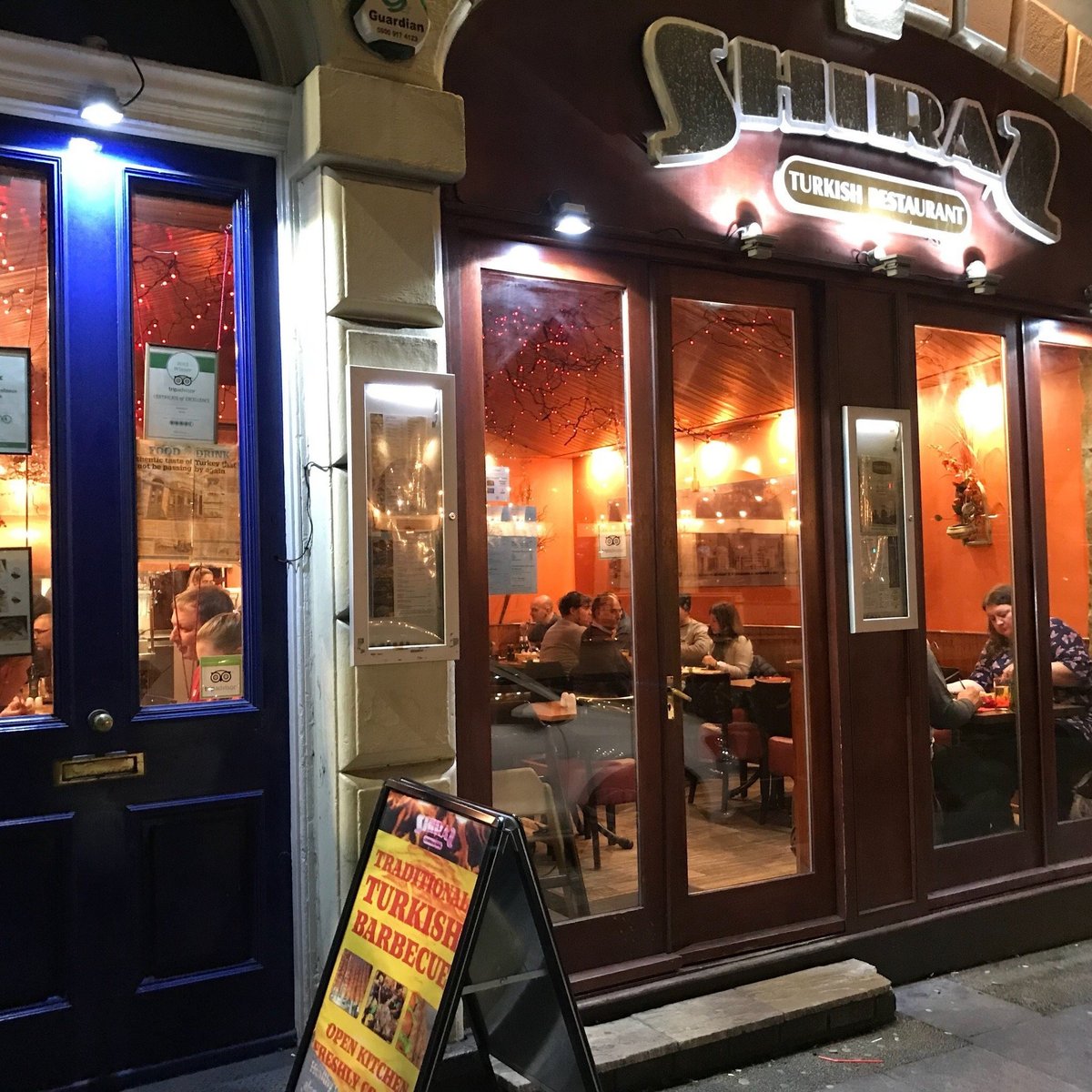 Shiraz Turkish Restaurant entrance at night, with warm lighting and a traditional barbecue sign on the pavement.