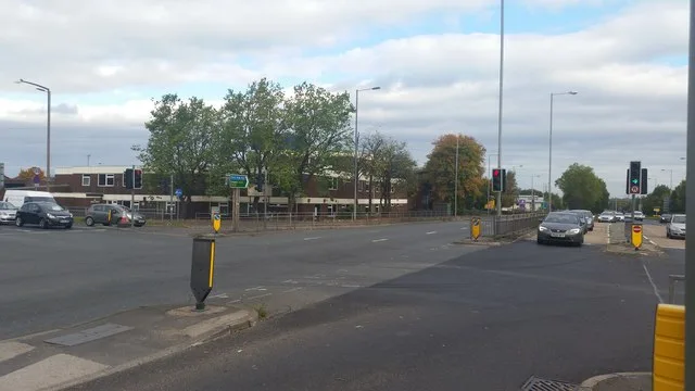 A wide junction on Dunnings Bridge Road in Netherton with traffic lights, cars and low commercial buildings