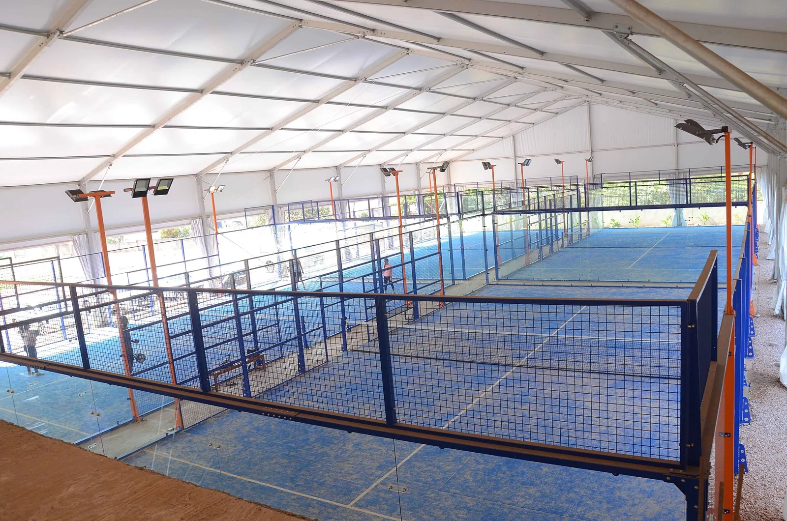An empty covered padel court with glass walls, mesh fencing and floodlights