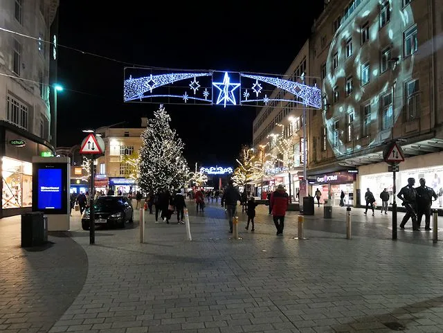Church Street in Liverpool at night with a lit Christmas tree, a star-shaped light display strung across the street and shoppers walking beneath
