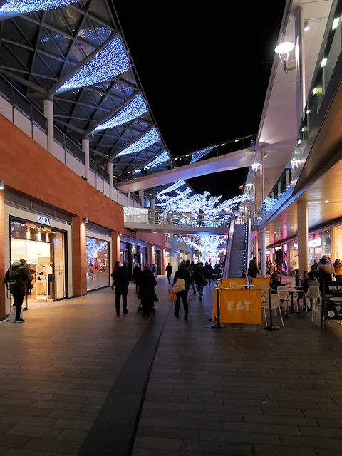 South John Street at Liverpool ONE at night, with white lights strung under the covered walkway and shoppers below