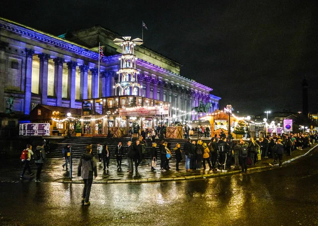 Liverpool Christmas Market on St George's Plateau at night, with lit stalls, a wooden Christmas pyramid and St George's Hall lit purple behind