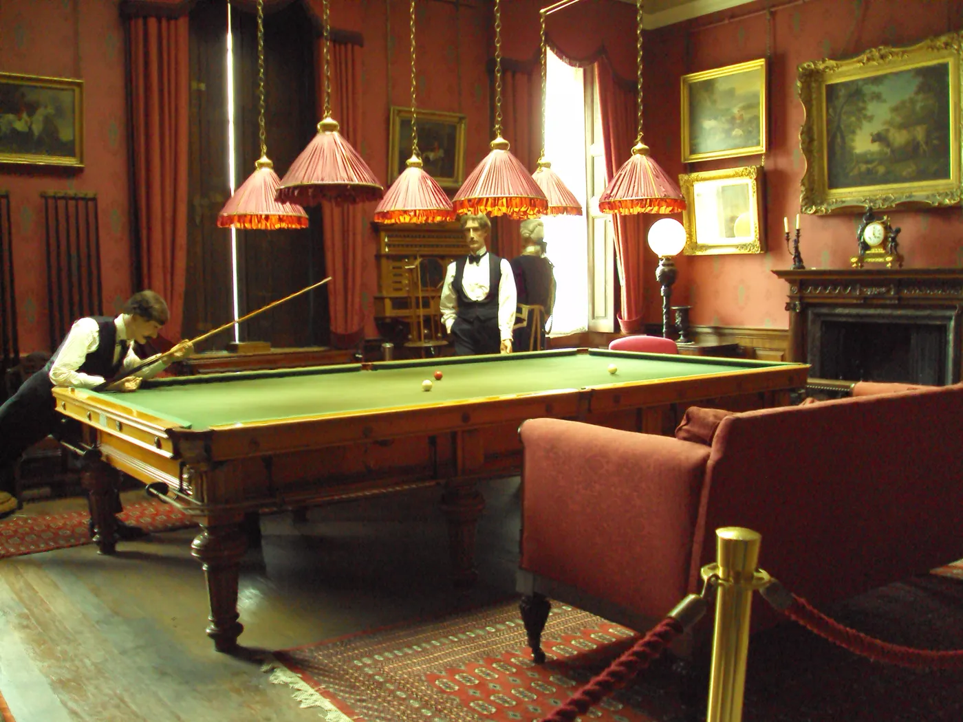 The billiard room at Croxteth Hall with a green baize table, red walls, oil paintings and costumed figures