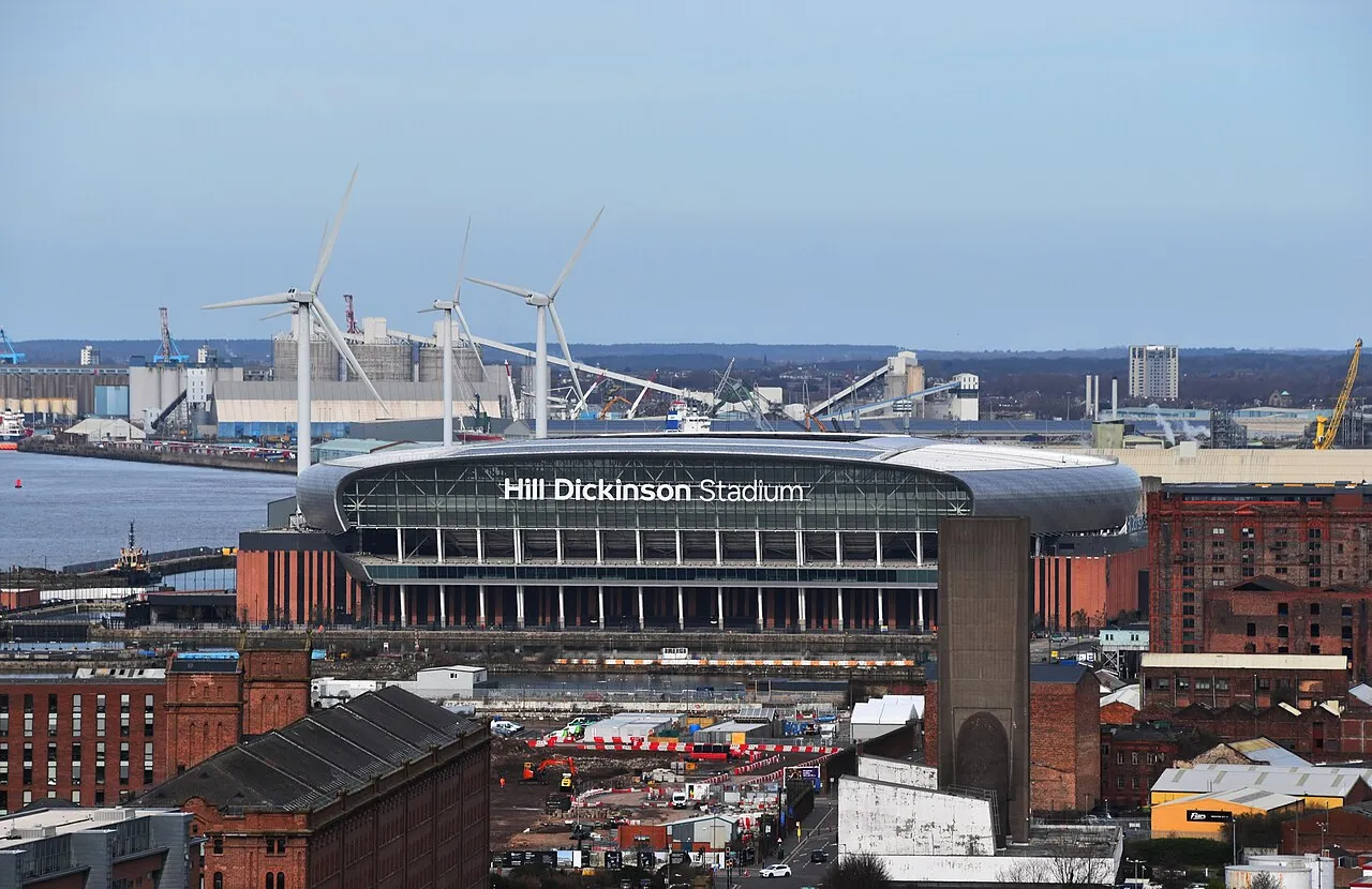 Hill Dickinson Stadium seen from above, with its name on the front and the Mersey and dock buildings behind it