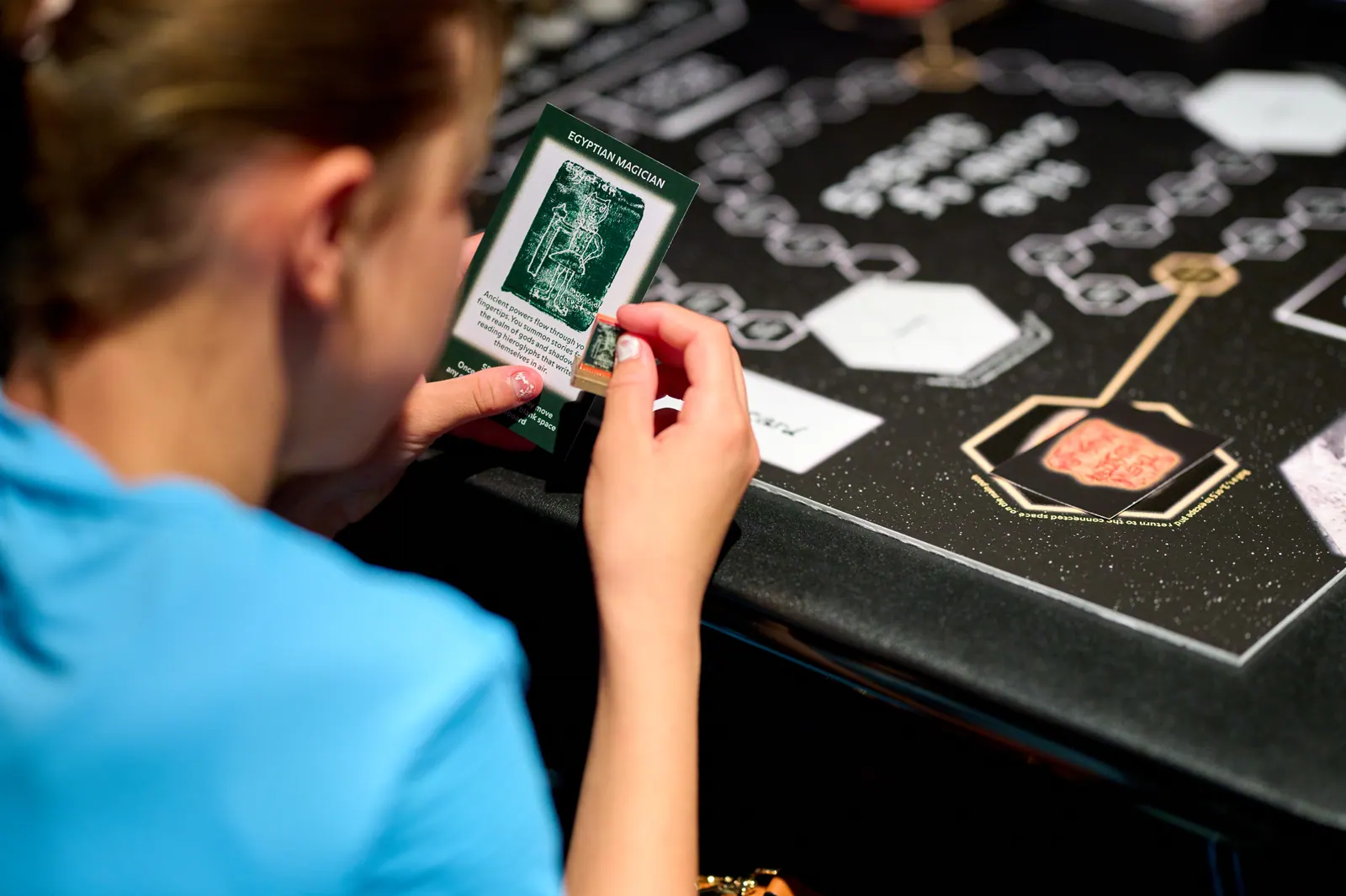 A young person holding a card over The Zone of Ghosts tabletop game