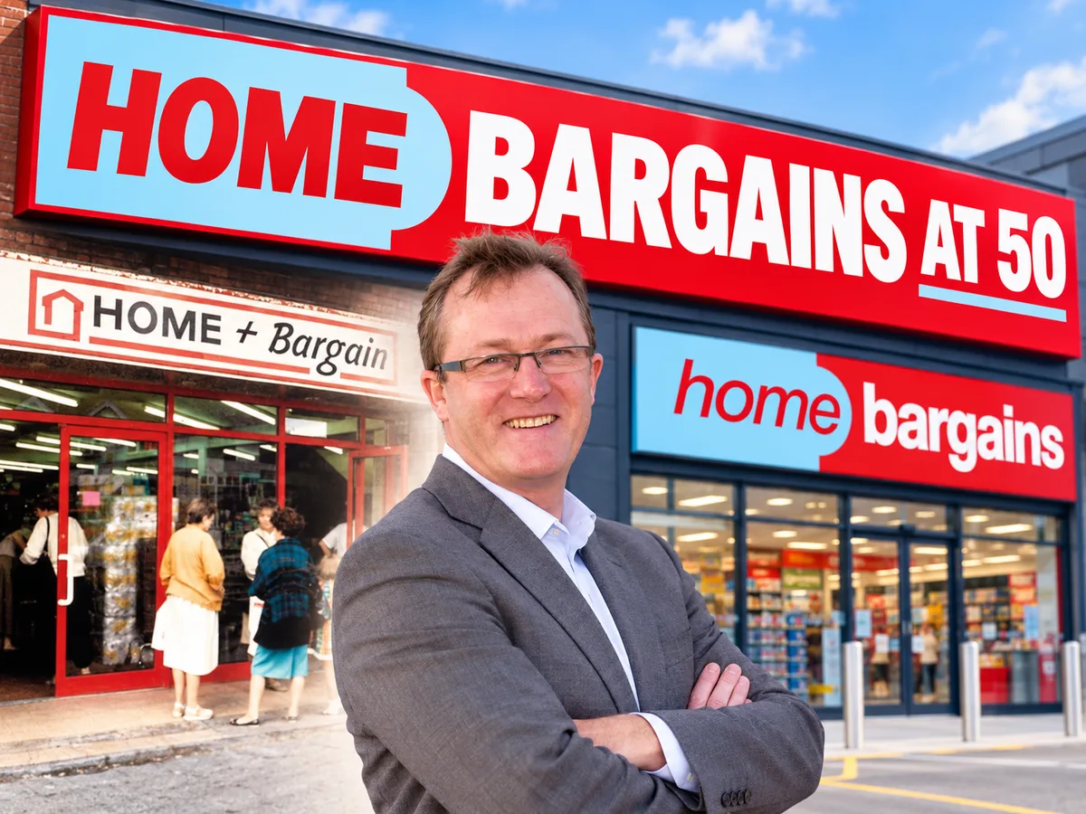 Smiling man in a grey suit with folded arms in front of a Home Bargains at 50 sign, beside an older Home + Bargain shop front.