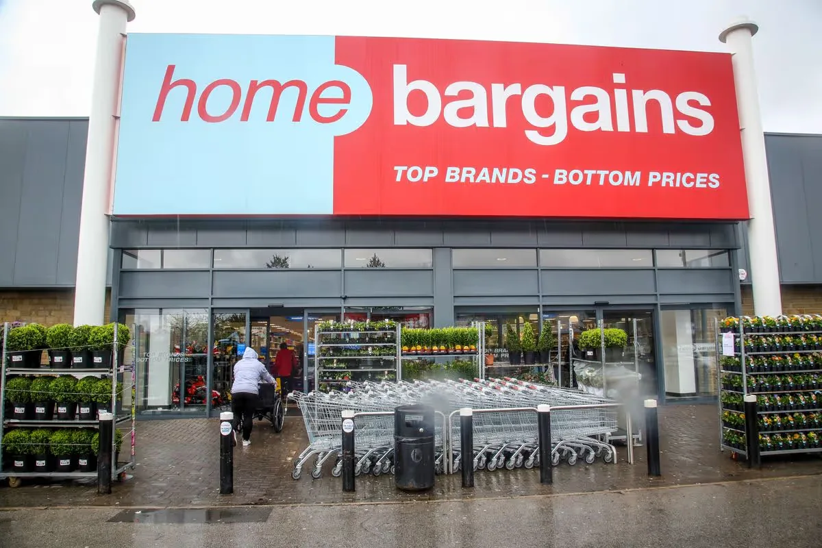 Home Bargains store front with a red and blue sign and the words Top Brands, Bottom Prices, with trolleys outside.