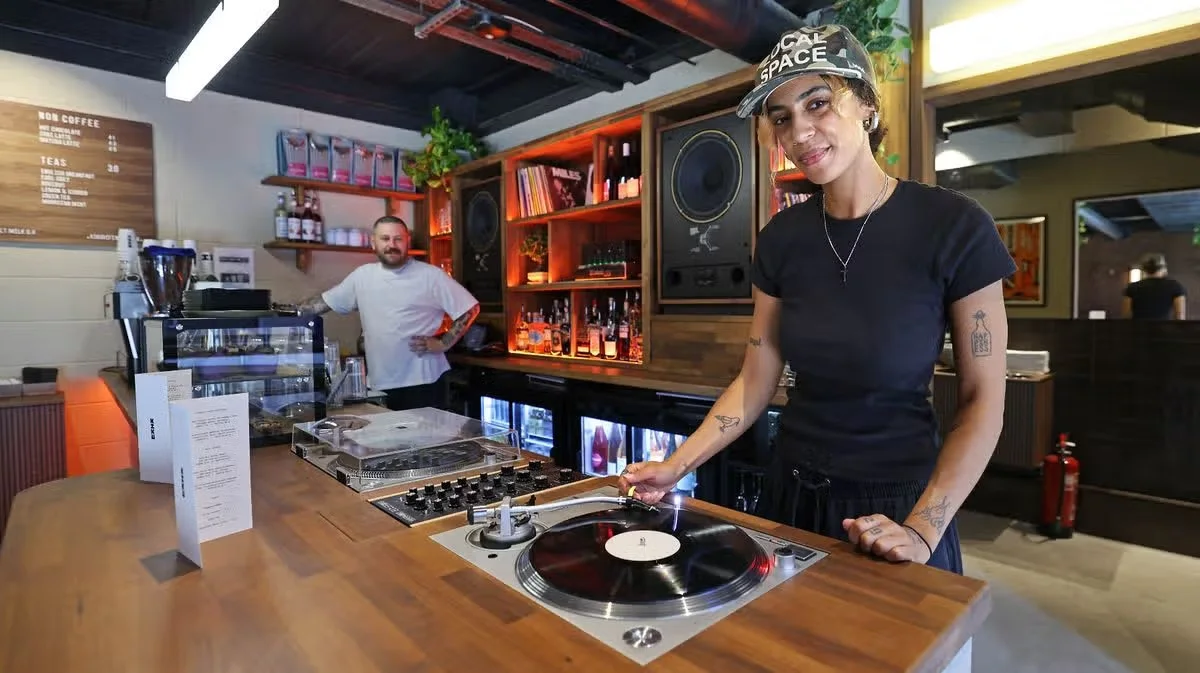 A member of staff cueing a record on a turntable at the Kiku Hifi bar, with speakers and shelved records behind