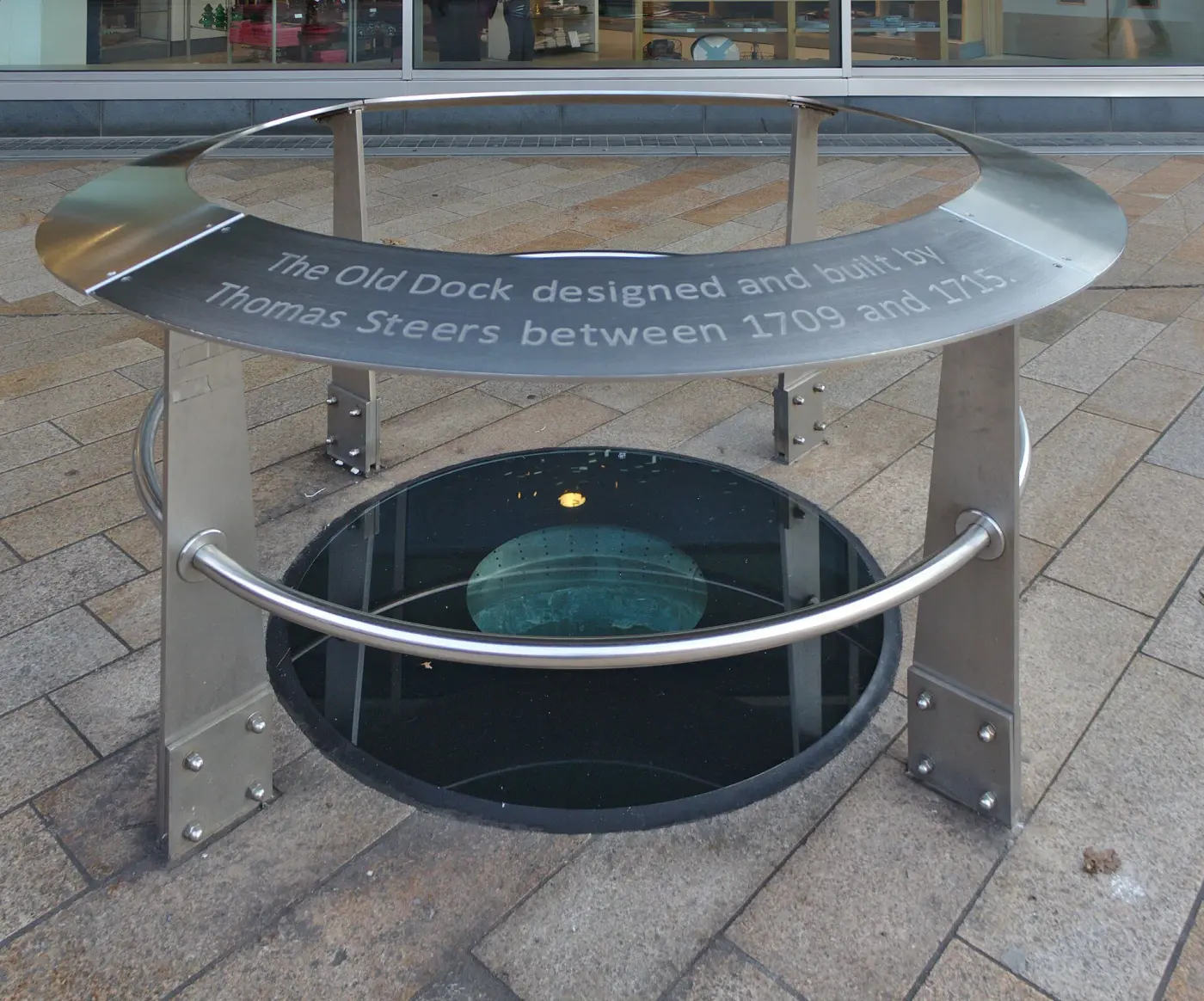 A glass viewing panel set into a paved city street, looking down onto the excavated brick wall of Liverpool's Old Dock
