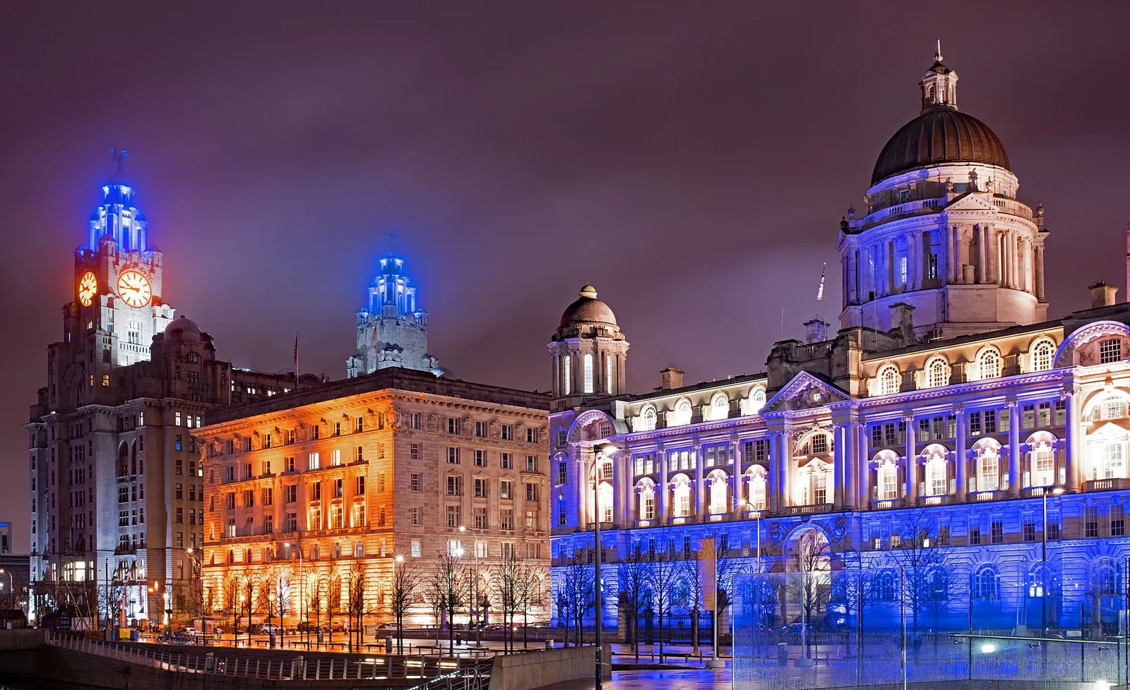 The Royal Liver, Cunard and Port of Liverpool buildings lit up in blue and orange at night on the Pier Head
