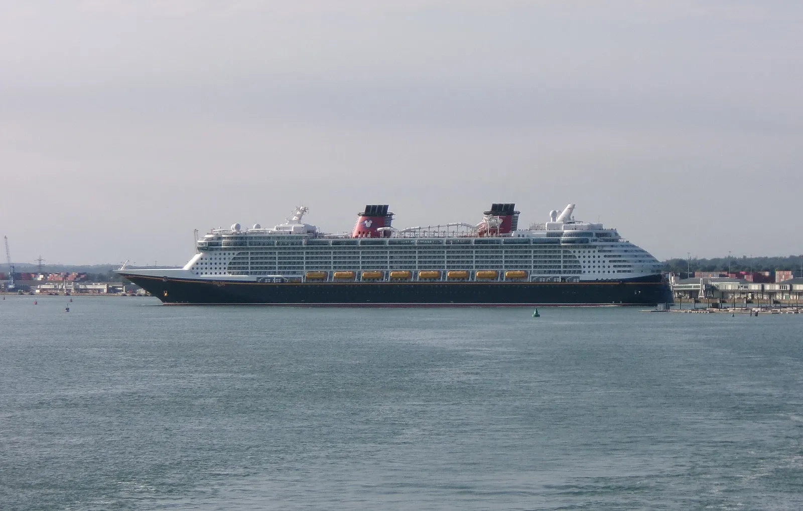 The cruise ship Disney Dream turning in Southampton Water, showing its dark hull and two red funnels