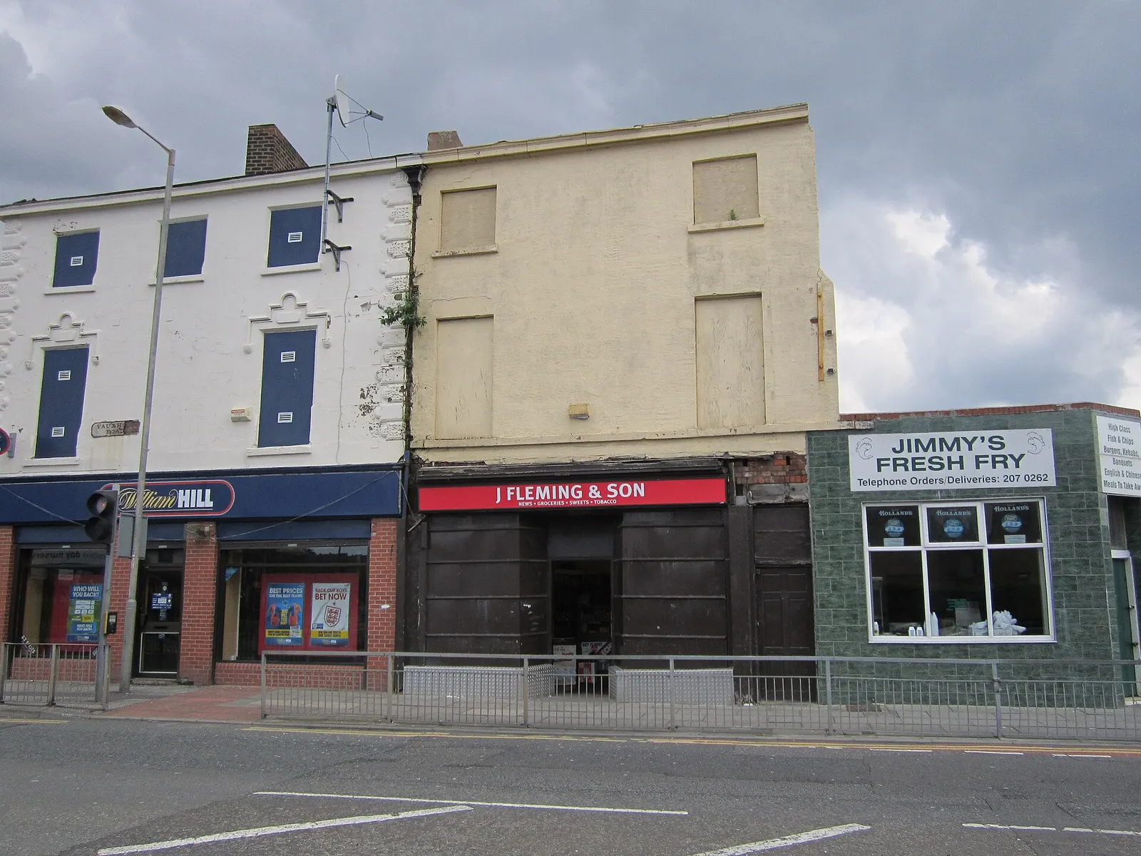 A row of shops on Vauxhall Road in 2012, including a bookmaker, a newsagent and a chip shop behind roadside railings