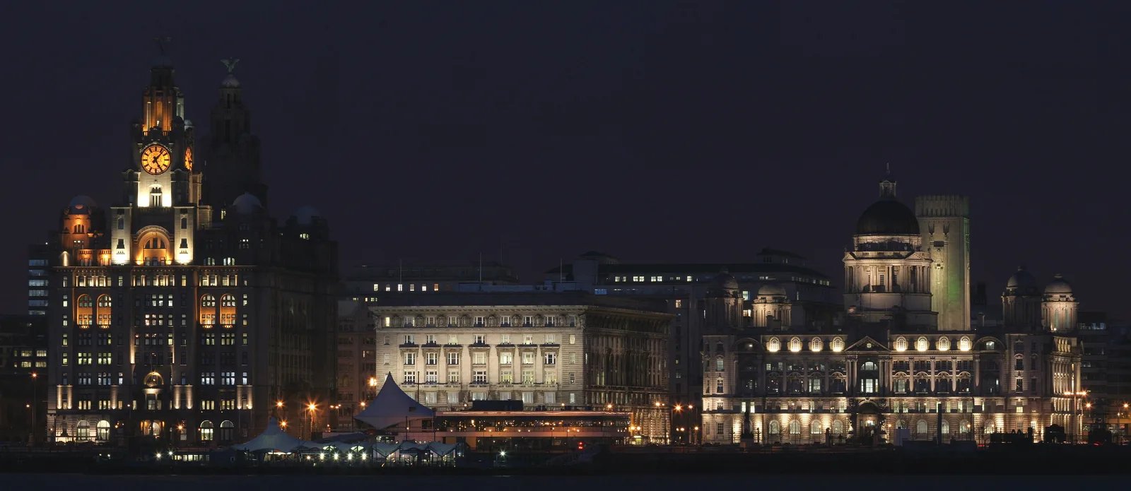 The Royal Liver Building, Cunard Building and Port of Liverpool Building lit up at night, seen from across the Mersey