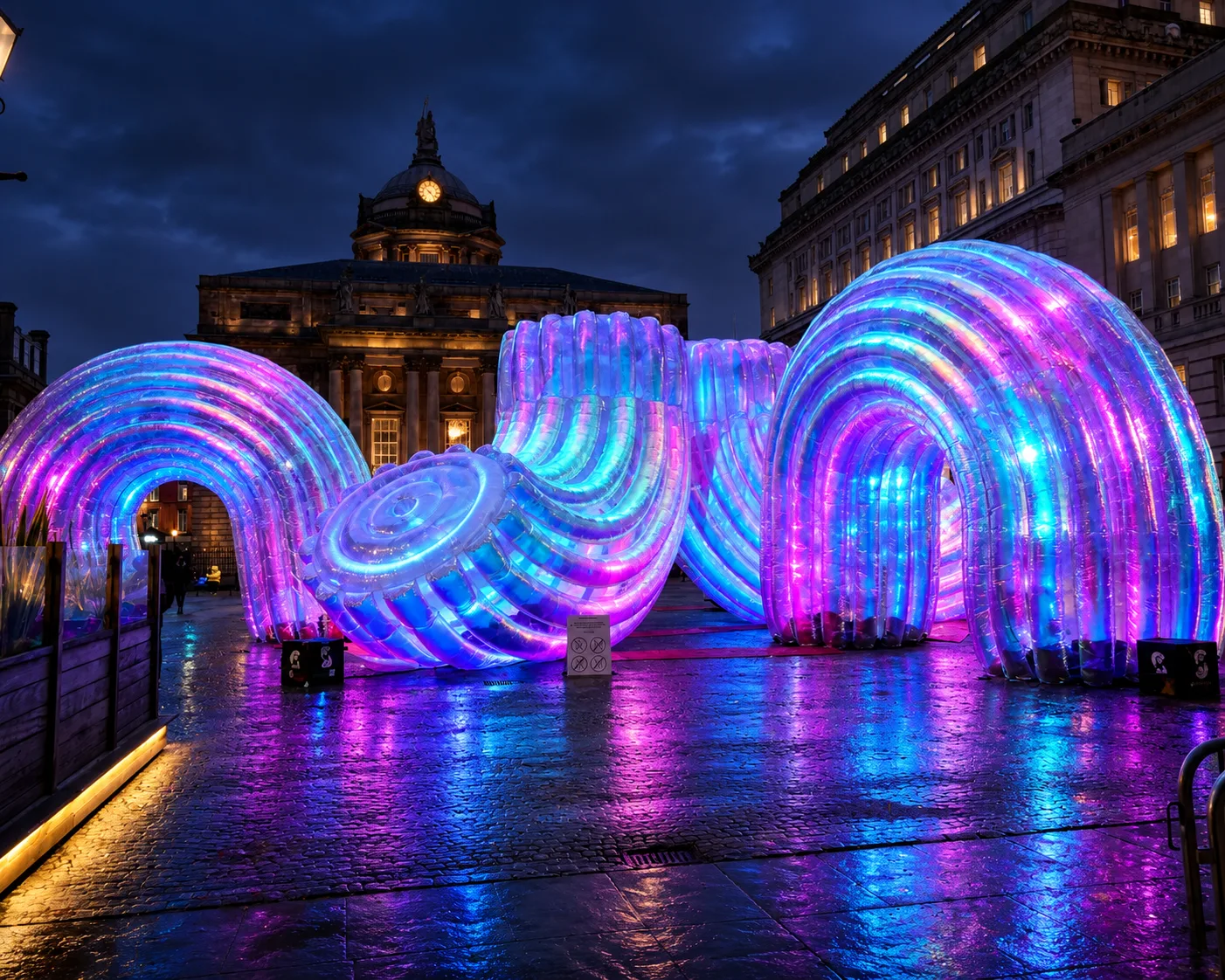 Glowing purple and blue inflatable arches on wet paving in front of Liverpool Town Hall at night