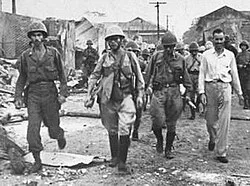Armed soldiers walking along a damaged street
