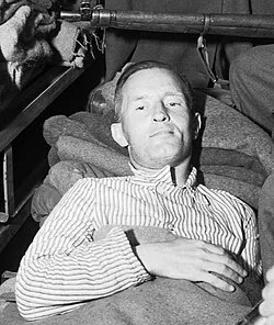 A wounded man in a striped shirt lying on a stretcher