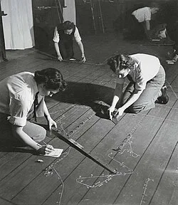 Wrens kneeling on a wooden floor, chalking out a tactical plot