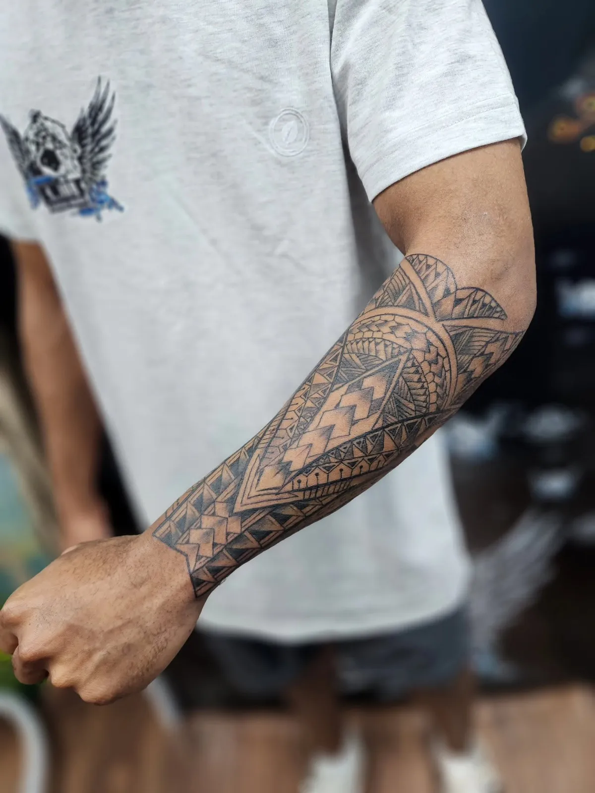 A black-ink geometric forearm tattoo with layered triangle and leaf patterns running from wrist to elbow