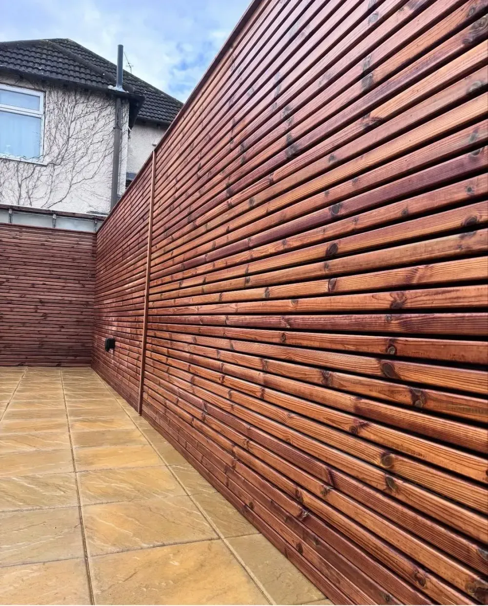 Horizontal timber slatted screen fence beside a sandstone patio in a back garden